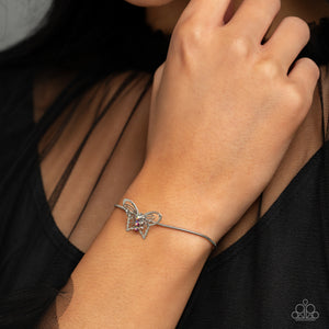 A deceptively simple silver butterfly charm glides along a silver snake chain for a whimsical flair along the wrist. Dainty, pink rhinestones, brushed in a UV shimmer, encrust along the butterfly's body, creating an understated shimmer, while intricate, airy wings fold out from the sparkle, adding a 3D effect to the design. Features an adjustable sliding knot closure. Due to its prismatic palette, color may vary.  Sold as one individual bracelet.