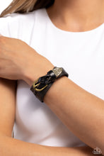 Load image into Gallery viewer, Featuring a weathered finish, a black leather band loops around the wrist in a belt loop fashion. Featured at the end of the loop, the leather braids into a brass cap fitting, embossed with a coat of arms style filigree for an urban statement. Features an adjustable belt loop closure.  Sold as one individual bracelet.
