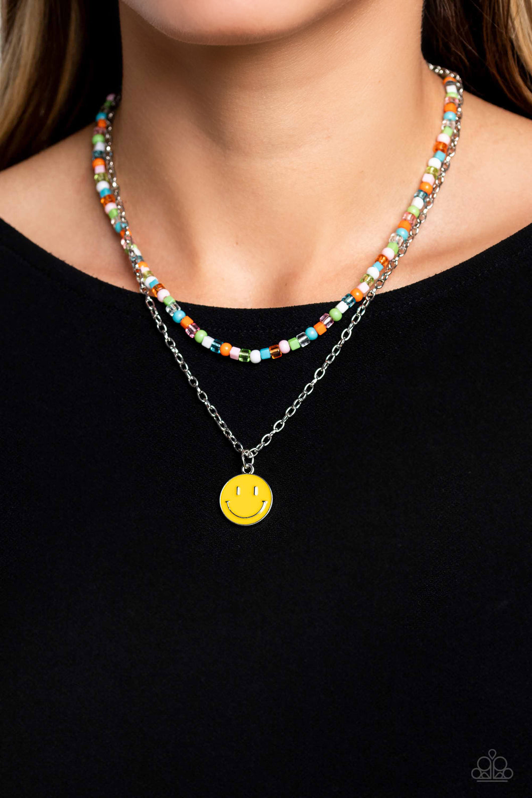 Gliding from a dainty, silver chain, a smiley face pendant stands out against a yellow backdrop. Completing the charismatic ensemble, a collection of seed beads in shades of baby pink, apple green, white, orange, and turquoise create bright pops of color around the neckline for a youthful finish. Features an adjustable clasp closure.  Sold as one individual necklace. Includes one pair of matching earrings.