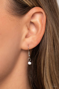 A small dainty white bead dangling from a silver fish hook earring.