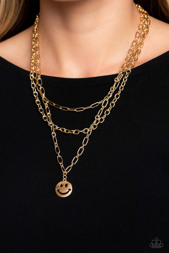 A trio of gold paperclip, classic, and oval link chains coalesces down the neckline for a monochromatic masterpiece. Strung on the lowermost oval link chain, a gold smiley face pendant, with a star mimicking a wink for one of its eyes, stands out and reflects light in every direction for a statement finish. Features an adjustable clasp closure.   Sold as one individual necklace. Includes one pair of matching earrings.