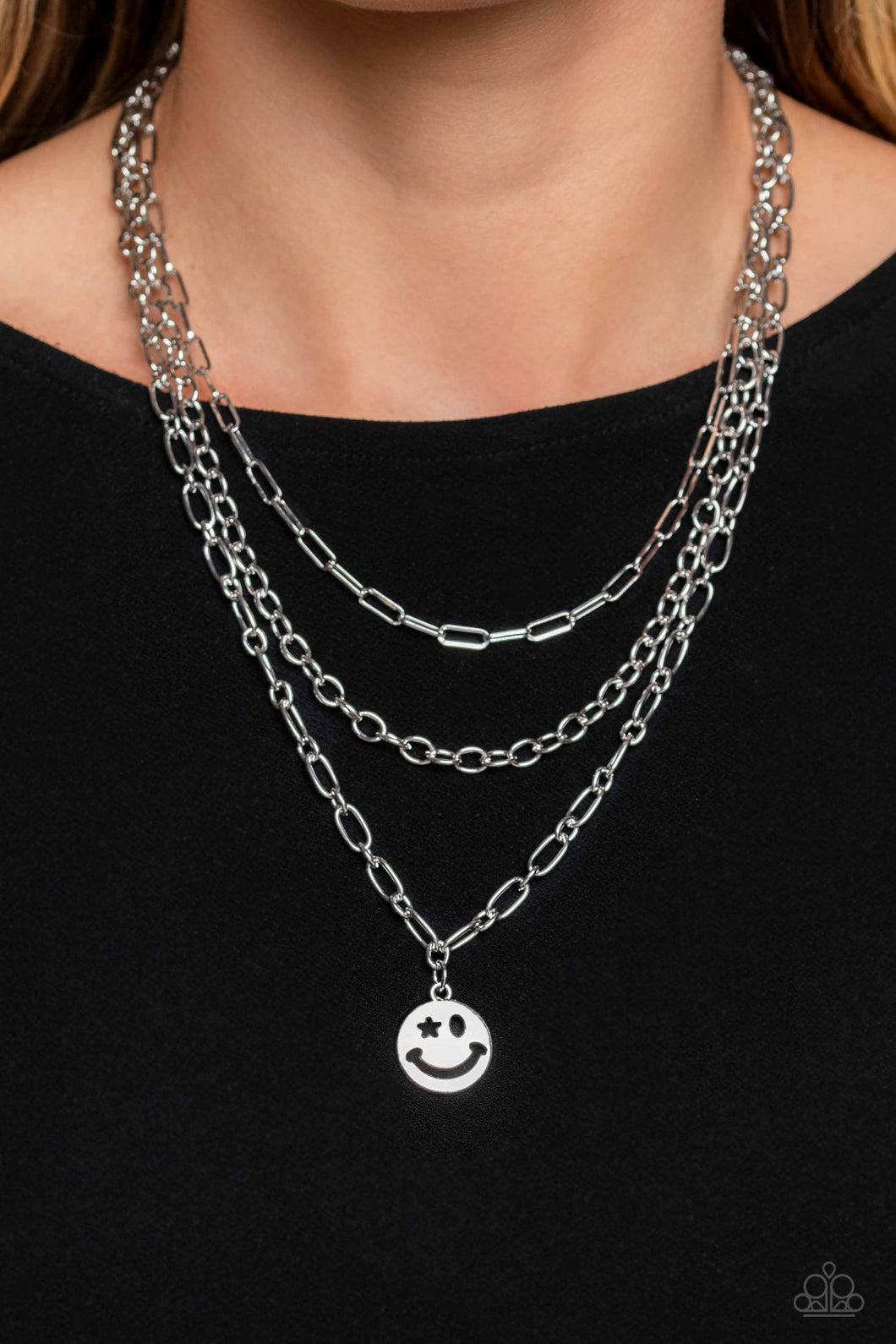 A trio of silver paperclip, classic, and oval link chains coalesces down the neckline for a monochromatic masterpiece. Strung on the lowermost oval link chain, a silver smiley face pendant, with a star mimicking a wink for one of its eyes, stands out and reflects light in every direction for a statement finish. Features an adjustable clasp closure.     Sold as one individual necklace. Includes one pair of matching earrings.