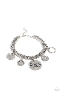 A collection of refined charms add some texture and shimmer to this monochromatic mash-up. An oversized, hammered disc is stamped with the phrase "be still" with the scripture reference "Psalm 48:10" listed underneath it. A smaller, hammered disc with a sprinkle of white rhinestones in its center and a silver disc featuring a scalloped ring in its center glide next to the oversized silver disc. A silver ring with serrated texture, and a silver disc with hammering and ring of white rhinestones glimmers. 