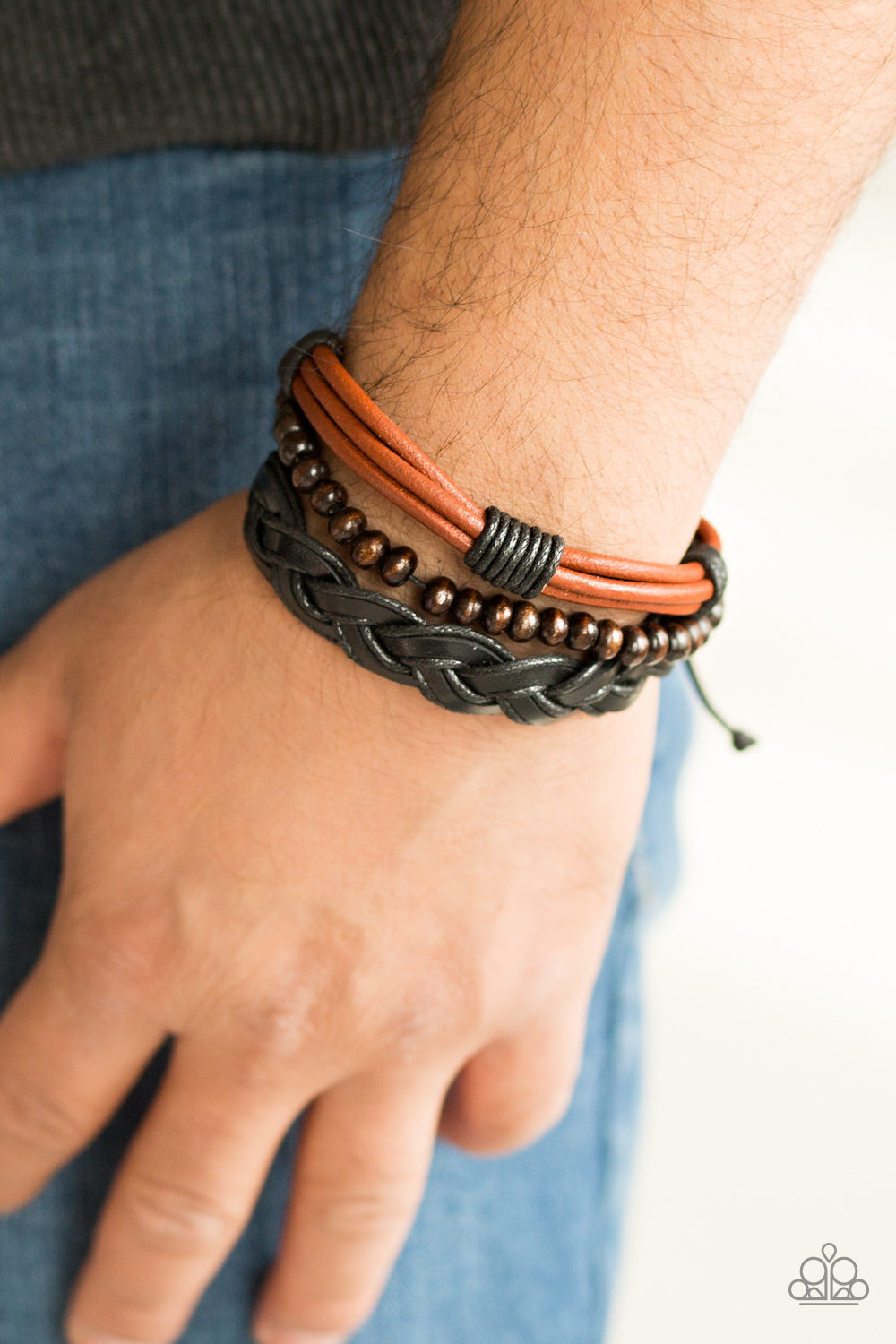 A mishmash of black braided twine and leather and strands of shiny brown leather cording layer across the wrist. A strand of wooden beads is added to the urban palette for an earthy finish. Features an adjustable sliding knot closure. Sold as one individual bracelet.