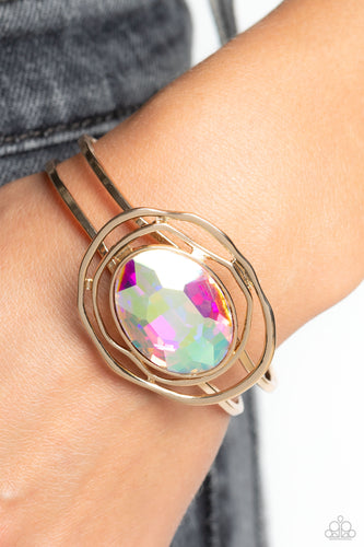 Featured in the center of airy, shiny gold bands, an oversized, faceted iridescent oval gem rests atop the wrist for a dazzling pop of color. Warped, shiny gold rings seemingly float around the sparkly gem for a whimsical finish. Features a hinged closure. Due to its prismatic palette, color may vary.  Sold as one individual bracelet.