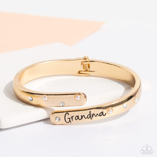 High-sheen gold curves into a hinged closure around the wrist. Featured on the upper curve, dainty pearls and white rhinestones alternate in a zig-zag pattern for a refined shimmer. The lower curve of gold features the stamped word 