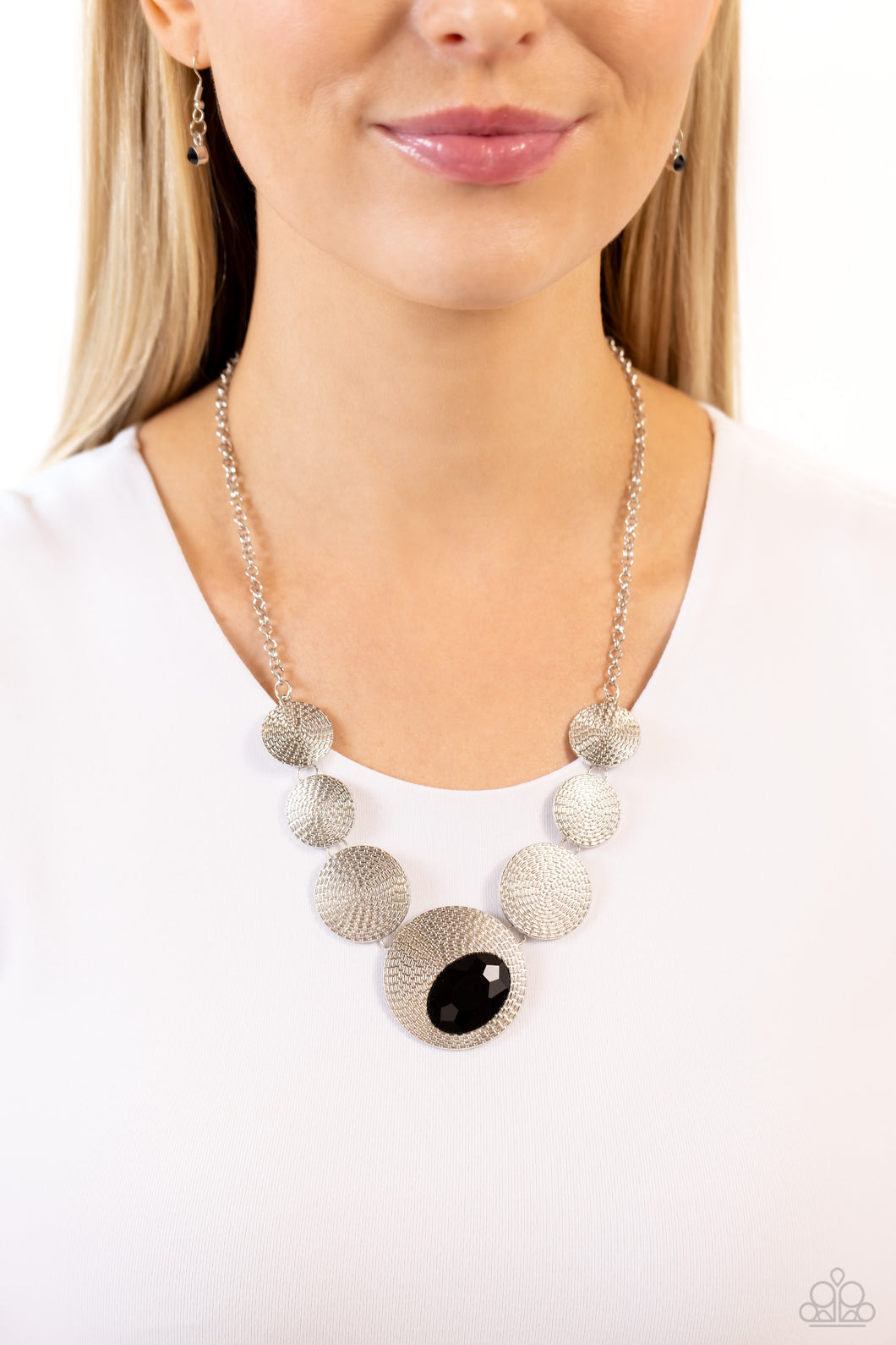 Embossed in an elongated dotted motif, a rustic collection of silver discs in varying sizes ruggedly links below the collar for an artisan inspired fashion. A faceted, oval, black gem sits at an angle on the biggest disc for a dauntless pop of color against the neckline. Features an adjustable clasp closure.  Sold as one individual necklace. Includes one pair of matching earrings.