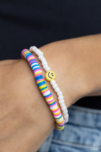 Hot pink, blue, white, and yellow clay discs combine with a strand of white seed beads to provide a vibrant pop of color along the wrist. Sporadically dotted in the high-sheen seed bead strand, yellow smiley face beads rest for a youthful finish on elastic stretchy bands.  Sold as one set of two bracelets.