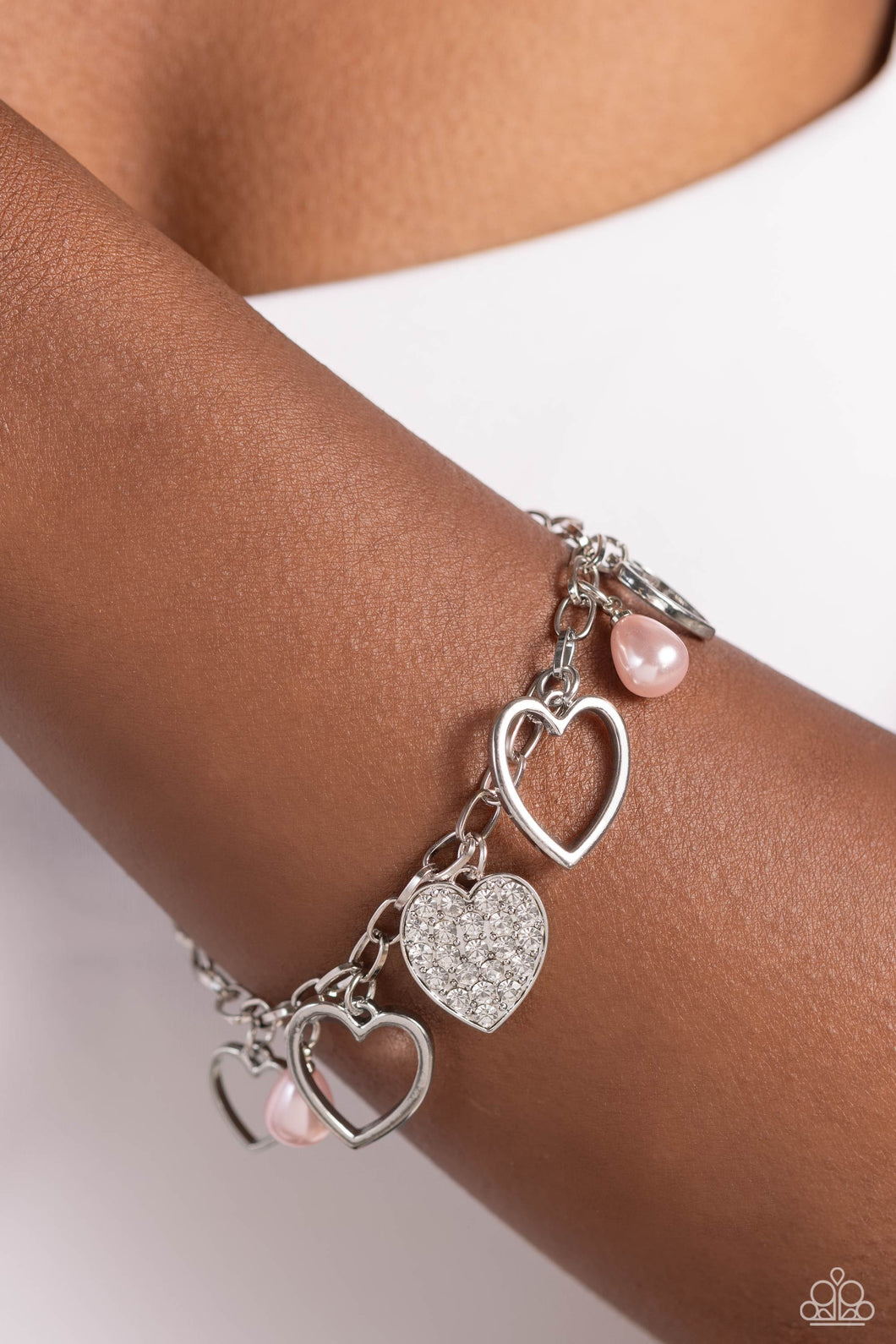 Glistening silver heart silhouettes, baby pink potato pearls, and a white rhinestone-encrusted silver heart frame dangle from a classic silver chain link around the wrist, resulting in a romantic fringe. Features an adjustable clasp closure.  Sold as one individual bracelet.
