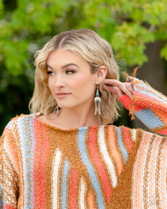 A turquoise stone pressed in a studded triangular fitting, and a silver floral-decorated half moon frame link into an earthy lure. A collection of daintily textured silver tassels in varying sizes swing from the bottom of the stacked frame for a whimsical finish. Earring attaches to a standard fishhook fitting. As the stone elements in this piece are natural, some color variation is normal.  Sold as one pair of earrings. Earrings are on a model.