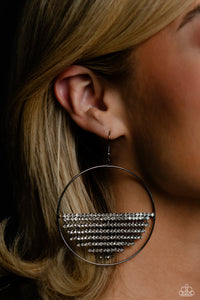 A curtain of white rhinestones is stretched between the edges of a skinny, oversized gunmetal hoop, creating a shimmering display. The rhinestones taper towards the center as they sway and cascade, adding sparkly movement for a fierce industrial finish. Earring attaches to a standard fishhook fitting.  Sold as one pair of earrings.