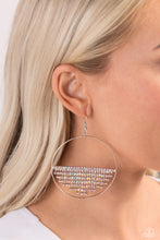 Load image into Gallery viewer, A curtain of iridescent rhinestones is stretched between the edges of a skinny, oversized silver hoop, creating a shimmering display. The rhinestones taper towards the center as they sway and cascade, adding sparkly movement for a fierce industrial finish. Earring attaches to a standard fishhook fitting. Due to its prismatic palette, color may vary.  Sold as one pair of earrings.
