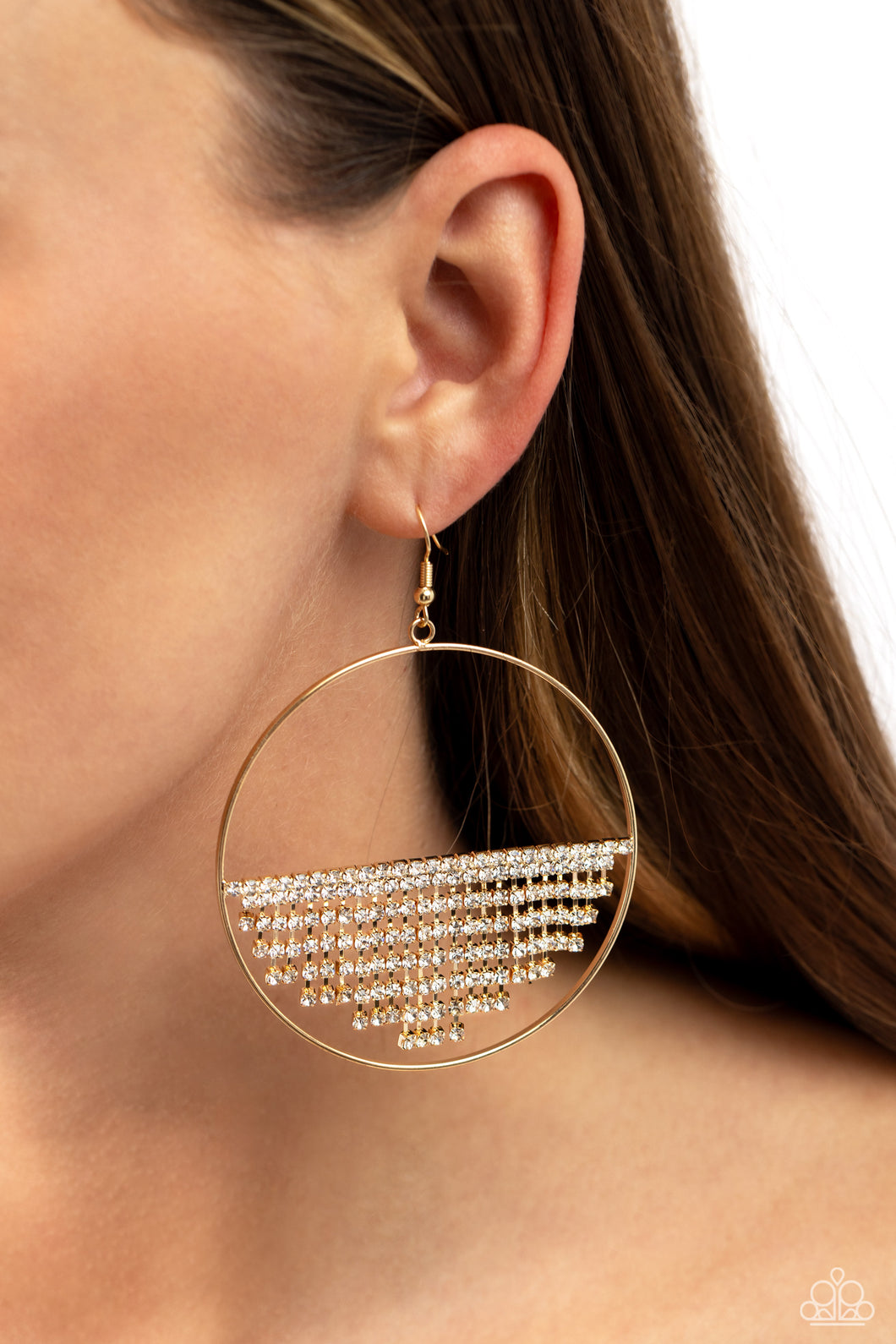 A curtain of white rhinestones is stretched between the edges of a skinny, oversized gold hoop, creating a shimmering display. The rhinestones taper towards the center as they sway and cascade, adding sparkly movement for a fierce industrial finish. Earring attaches to a standard fishhook fitting.  Sold as one pair of earrings.