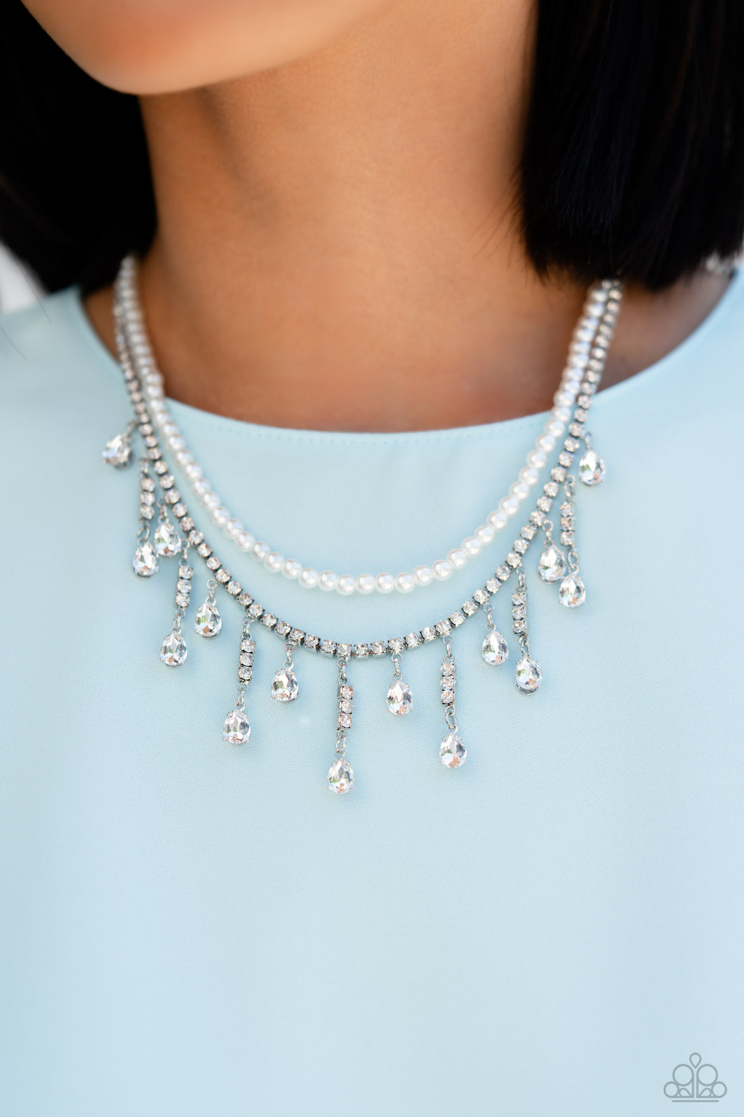 Featuring a white rhinestone square-fitting chain, white teardrop-cut gems, bordered in silver pronged fittings, swing from streams of glittery rhinestones while solitaire teardrop gems drip in an alternating pattern. A strand of gleaming white pearls layers above the silver display for a luxurious finish around the collar. Features an adjustable clasp closure.  Sold as one individual choker necklace. Includes one pair of matching earrings.