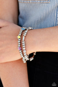 A strand of textured, cylindrical, and round high-sheen silver beads combine with a single strand of silver beads, sporadically infused with vivacious charm beads to create an energetic stack of stretchy bracelets. The colorful beaded stack features a yellow star, blue lightning bolt, green money bag, orange tropical flower, red lips, blue and green earth, pink and purple flower, and a pink heart charm with the words "love me" for a youthful finish.  Sold as one set of two bracelets.