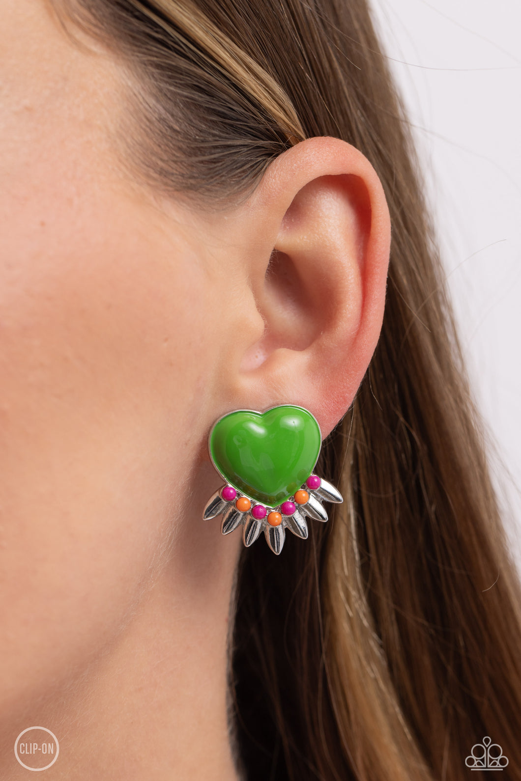A Classic Green heart pressed in a sleek silver frame stands out at the ear. Textured silver leaves flare out from a curved cluster of Rose Violet and orange seed beads that adorn the bottom of the heart display, creating a spring-inspired fringe. Earring attaches to a standard clip-on fitting.  Sold as one pair of clip-on earrings.