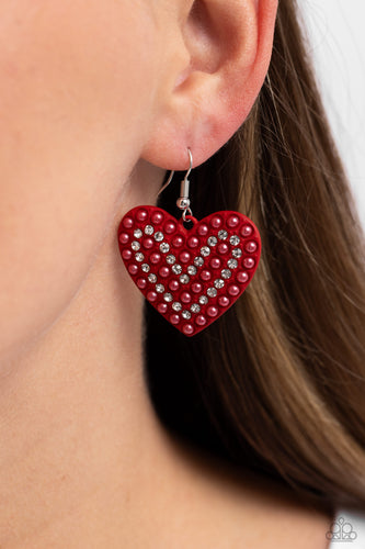 A red-painted heart is covered in rows of tiny white rhinestones and red pearls, emitting radiant shimmer as it swings from the ear. Earring attaches to a standard fishhook fitting. Sold as one pair of earrings.