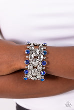 Load image into Gallery viewer, A collection of hammered oval silver beads, sleek silver beads, and blue UV beads are threaded along stretchy bands around the wrist, creating a zigzag pattern of edge. Due to its prismatic palette, color may vary.   Featured inside The Preview at Made for More! Sold as one individual bracelet.
