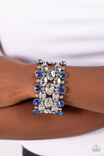A collection of hammered oval silver beads, sleek silver beads, and blue UV beads are threaded along stretchy bands around the wrist, creating a zigzag pattern of edge. Due to its prismatic palette, color may vary.   Featured inside The Preview at Made for More! Sold as one individual bracelet.