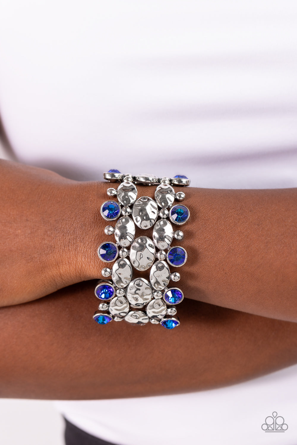 A collection of hammered oval silver beads, sleek silver beads, and blue UV beads are threaded along stretchy bands around the wrist, creating a zigzag pattern of edge. Due to its prismatic palette, color may vary.   Featured inside The Preview at Made for More! Sold as one individual bracelet.