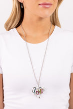Load image into Gallery viewer, Featuring blue, fuchsia, olive, and rose rhinestones, the word &quot;LOVE&quot; floats inside an oversized, airy heart-shaped frame as it sways from a lengthened silver chain for a Valentine&#39;s-inspired centerpiece. Features an adjustable clasp closure. Sold as one individual necklace. Includes one pair of matching earrings. 
