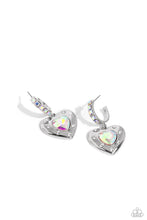 Load image into Gallery viewer, Featuring an iridescent shimmer, an iridescent heart gem is pressed into an antiqued silver heart frame adorned in white rhinestones. The antiqued heart sways from the bottom of a thick silver hoop encrusted in square iridescent gems resulting in a whimsical fashion. Earring attaches to a standard post fitting. Hoop measures approximately 3/4&quot; in diameter. Due to its prismatic palette, color may vary.  Sold as one pair of hoop earrings.
