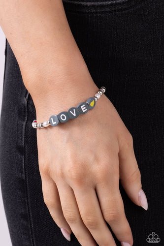 Infused on an elastic stretchy band, white pearls, gray, hot pink, and yellow seed beads, silver studs, and gray beads spelling out the word 