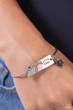 Load image into Gallery viewer, The word &quot;BeYOUtiful&quot; is stamped across a thick plate of silver, with the &quot;YOU&quot; in a playful orange font. A textured, silver lotus flower charm gathers at the side of the inspirational centerpiece as it connects to a skinny silver bar that wraps around the wrist. Features a hook and eye closure.  Sold as one individual bracelet.
