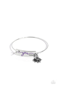 The word "Beyoutiful" is stamped across a thick plate of silver, with the "you" in a playful purple font. A textured, silver lotus flower charm gathers at the side of the inspirational centerpiece as it connects to a skinny silver bar that wraps around the wrist. Features a hook and eye closure.  Sold as one individual bracelet.