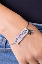 Load image into Gallery viewer, The word &quot;Beyoutiful&quot; is stamped across a thick plate of silver, with the &quot;you&quot; in a playful purple font. A textured, silver lotus flower charm gathers at the side of the inspirational centerpiece as it connects to a skinny silver bar that wraps around the wrist. Features a hook and eye closure.  Sold as one individual bracelet.
