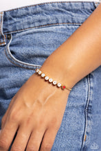 Load image into Gallery viewer,  Delicately attached to a dainty gold box chain, thick circular gold fittings spell out the word &quot;BELIEVE&quot; across a white-painted backdrop with red-painted hearts embellishing the ends of the word, creating a sleek inspiring display. Features an adjustable sliding bead closure.  Sold as one individual bracelet. 
