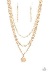 A trio of gold paperclip, classic, and oval link chains coalesces down the neckline for a monochromatic masterpiece. Strung on the lowermost oval link chain, a gold smiley face pendant, with a star mimicking a wink for one of its eyes, stands out and reflects light in every direction for a statement finish. Features an adjustable clasp closure.   Sold as one individual necklace. Includes one pair of matching earrings.
