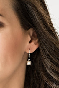 Small white pearl hanging from a silver fish hook earring.